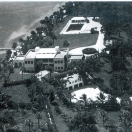 Aerial view of waterfront mansion, exterior buildings and pool