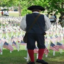 Man in period costume facing memorial markers with flags